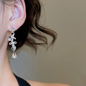 Detail of silver bow earrings with sparkling crystals and a teardrop-shaped zircon drop