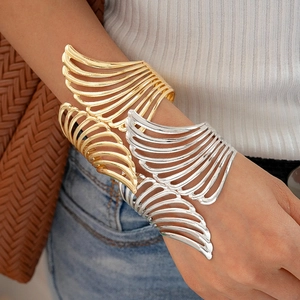 Close-up of gold and silver cutout wing bracelets on wrist with metallic luster