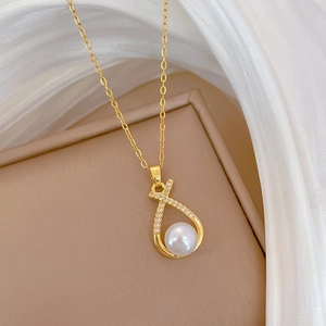 Close-up of golden necklace with a crisscross zircon pendant holding a white pearl