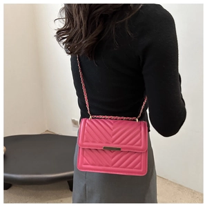 Model wearing a rose red quilted leather crossbody bag with golden chain and V-pattern