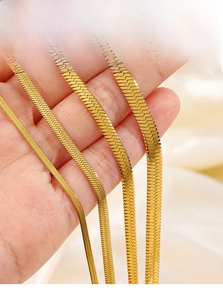 Detail view of four 18K gold plated snake bone chains in various widths held by hand