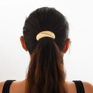 Detail view of a polished golden curved metal ponytail cuff worn on a minimalist hairstyle