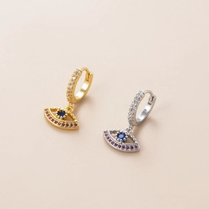 Gold- und Silberne Evil Eye Creolen mit blauen Zirkonia-Anhängern auf beige Hintergrund
