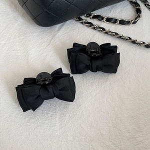 Paire de pinces à cheveux noeud en satin noir avec sac matelassé chic sur fond blanc