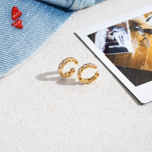 Detail shot of gold ear cuffs with white zircon stones on rustic background with denim