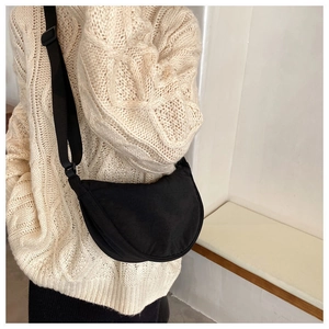 Minimalist black nylon crescent crossbody bag worn over a beige knit sweater in a clean interior