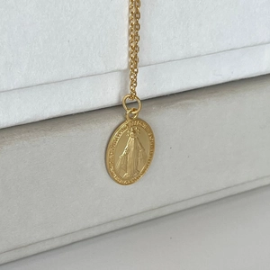 Macro shot of 925 sterling silver Virgin Mary oval relief pendant on gold cross chain