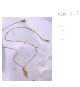 Detail of gold rose pendant necklace featuring K18 engraved tag on a minimalist background