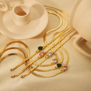 Gold-plated snake chain bracelets with colorful heart-shaped zircon stones on beige fabric