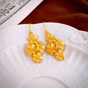 Detail of matte gold floral cluster earrings with five-petal flower design on white porcelain