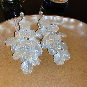 Macro detail of elegant cream flower tassel earrings with golden hooks in a ceramic dish