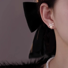 Close-up of model wearing elegant silver bow earrings with zircon and dangling pearls
