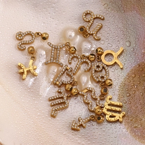 Macro view of 18K gold-plated zodiac charms with micro-pave zircons on a wet pearl surface
