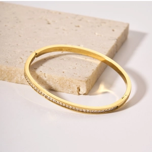 Dettaglio del bracciale in titanio dorato con zirconi bianchi su supporto in pietra