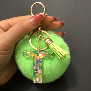 Close-up of green pompom keychain with resin letter T and heart-shaped sequins