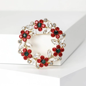 Macro shot of gold floral wreath brooch with red and green rhinestones on white base