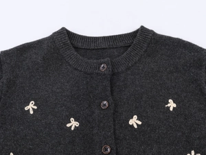 Detail view of bow embroidery and vintage buttons on dark grey knit cardigan sweater