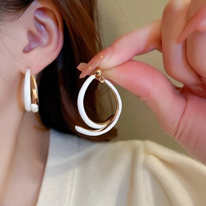 Gros plan d'une boucle d'oreille géométrique torsadée blanc crème et dorée