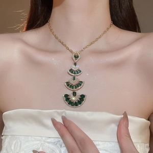 Detailed close-up of a layered fan pendant necklace with green stones on a model