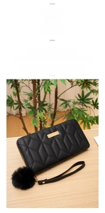 Detail of black quilted long wallet with golden zipper and fluffy pompom keychain