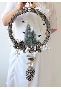 Close-up of handmade Christmas wreath with white berries and pine cones held by hands