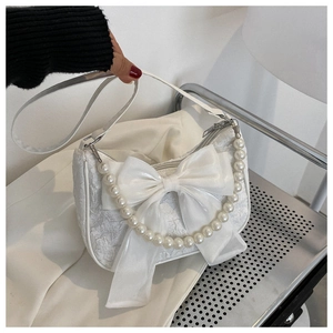 Close-up of white pleated handbag featuring a large bow and elegant pearl handle strap