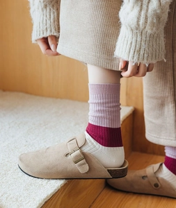 Detail of striped ribbed cashmere socks paired with beige suede clogs on wood floor