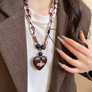 Detail of vintage heart pendant with saturn logo on checkered woven beaded necklace