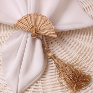 Handwoven rattan fan-shaped napkin ring with golden tassel on white napkin