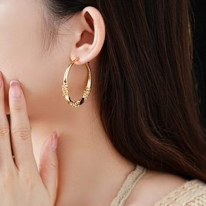 Close-up of golden twisted hoop earrings with embossed texture on female model