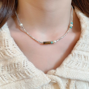 Detailed close-up of tiger eye and pearl beaded silver necklace on a model
