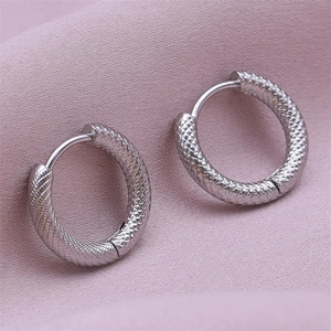 Macro detail of silver round earrings featuring snake scale texture and hinge closure