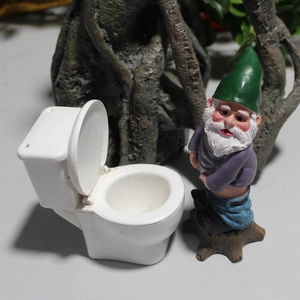 Funny garden gnome sitting on a miniature toilet made of resin for outdoor lawn decor