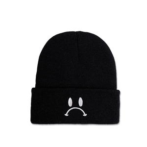 Détail du bonnet en maille noir avec broderie blanche visage triste sur le bord plié