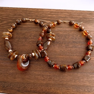 Detailed view of two bohemian beaded necklaces with amber charms on wood background