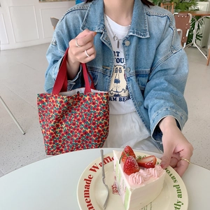 Floral corduroy handbag detail with red handles and vintage pattern shown in a cafe