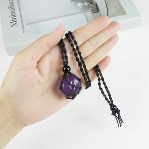 Handheld detail of a raw purple crystal pendant in black hand-woven rope mesh
