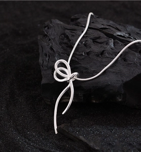 Detail shot of a silver bow pendant on a fine snake chain against black gravel