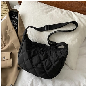Quilted black hobo bag with satin finish displayed on soft white pillow with blazer