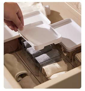Detail showing hand placing a white lid on a clear drawer organizer for socks
