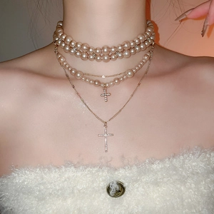 Detail of layered champagne gold necklace with pearl beads and sparkling cross pendants