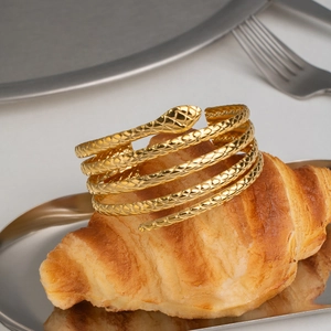 Close-up of golden snake wrap bracelet with textured scales displayed on a croissant