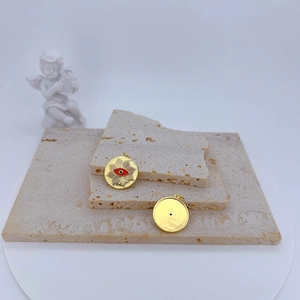 Retro gold-plated evil eye pendants with red enamel on beige stone display blocks