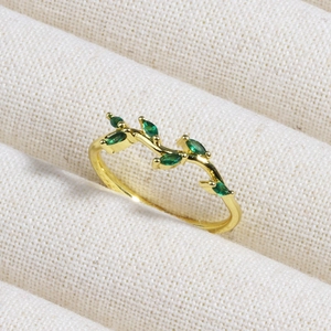 Detailed shot of golden branch ring with marquise emerald stones on beige fabric texture