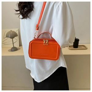 Fashionable bright orange PU leather crossbody bag with gold hardware worn by a model