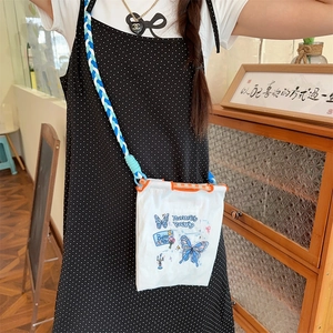 Détail du sac bandoulière en toile blanche avec broderie papillon bleu et sangle tissée
