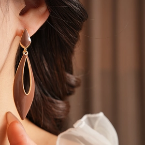Close-up of coffee brown enamel teardrop earrings with gold metal on model's ear