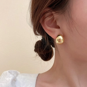 Close-up of golden teardrop earrings with a mirror finish on a model's earlobe