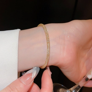 Gros plan d'un bracelet doré à texture maillée porté au poignet avec tenue chic