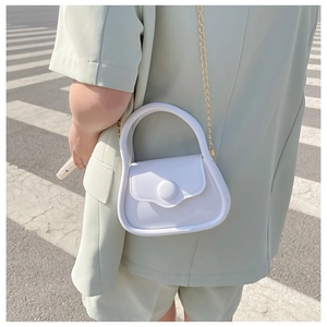 Close-up of a mini white macaron jelly bag with a gold chain strap on a crosswalk